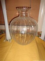 Clear round glass vase with vertical etched lines on yellow cloth surface with windows and tiled backsplash in background.