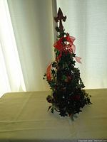 Full view of the decorative Christmas tree showing green holly-like leaves, red ribbon bow, and wooden fleur-de-lis topper.