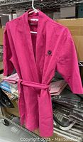 Front view of the pink bathrobe hanging showing the removable belt and pocket detail.