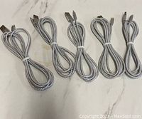 Five grey braided USB charging cables coiled on a white surface, showing USB and Lightning connectors clearly.
