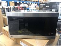 LG LMC1575ST microwave oven placed on cardboard boxes showing the front stainless steel and black glass door panel.