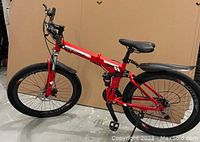 Full left side view of red folding bicycle showing frame, wheels, saddle, and kickstand