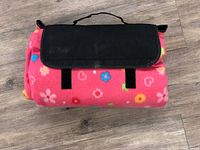 Rolled up picnic blanket secured with black flap and handle, showing pink fleece with floral pattern