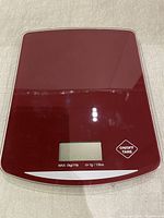 Top view of a red digital kitchen scale with tempered glass platform, LCD screen, and touch controls visible.