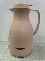 Side view of glossy light pink vacuum carafe with ergonomic handle and spout showing Thermotastic logo on body.