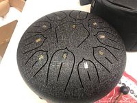Close-up top view of black steel tongue drum with 11 tone tongues marked with gold numbers shaped in petal-like cuts.