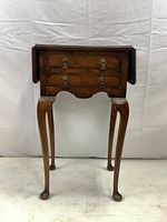 Front view of antique drop-leaf side table showing two drawers and Queen Anne legs.