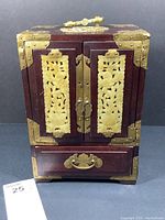 Front view of the wooden jewelry chest with jade panels on the doors and brass corner decorations.