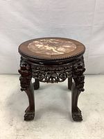 Front view of round carved wood plant stand with marble inset top and claw feet