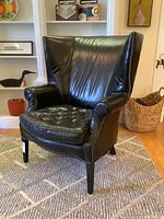 Front view of the black leather high-back armchair showing hobnail trim, tufted seat cushion, and tapered wood legs.