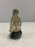 Front left diagonal view of the nude girl figurine seated on a stone base.