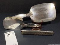 Photo of three pieces: hand mirror, hairbrush with silver back, and two combs, arranged on black background