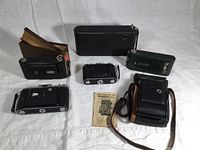 Overview of the 6 vintage cameras and accessories including a camera manual and black carrying case.