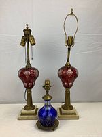Front view of the three lamps showing cranberry glass pair and blue decanter lamp with marble and brass bases