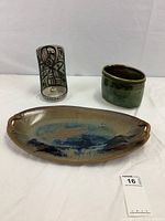 Full view of three pottery items: fish plate with decorative fish, green vase, and abstract-patterned candle holder.