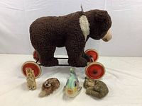 Side view of all five animals, large brown bear on wheels front and center with four smaller plush animals in front