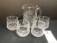 Pitcher and four glasses displayed together on black background