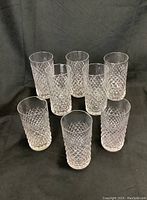 Eight crystal tumblers with diamond cut pattern arranged in rows on black backdrop.
