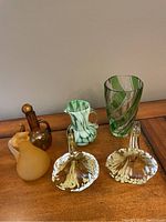 Photo showing six art glass pieces including a tall green striped vase, amber glass vase and pitchers, a white and green pitcher, and two amber and white flower shaped vases. Chip visible on green vase.