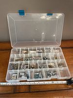 Plastic storage box open showing multiple compartments filled with assorted beads in metallic and crystal-like finishes.