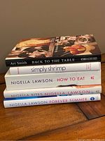 Side view of the stacked cookbooks showing titles and authors including Art Smith and Nigella Lawson
