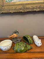 Photo of 4 ceramic and figurine items on a wooden table: fish figurine, green ceramic piece, white bunny dish, white pet treat bowl.
