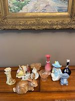 Photo showing the full collection of ceramic figurines, glassware, and vases arranged on a wooden surface beneath a framed painting.