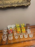 Full view of 17 mid century vintage glasses arranged on wood table under ornate frame