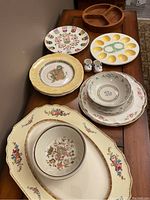 Photo showing assorted decorative plates with various floral and gold patterns, an egg plate, and a pair of salt and pepper shakers on table.