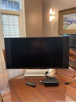 Front view of HP Envy 32 monitor on table with power cord and remote control visible.