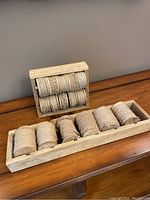 View of jute and burlap ribbon rolls placed in two wooden holders shown on a wooden surface against a gray wall