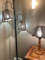 View of black tension pole lamp with two hanging rattan/wicker shades and table lamp with wooden base and rattan shade on hexagon wooden side table