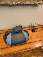 Top view of the black and gray neck massager with power cord and plug laid out on wooden surface.