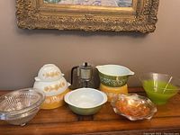 Overview of the lot showing all bowls, glassware and espresso maker on a wooden surface under framed artwork.