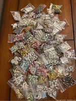 Photo showing overall assortment of plastic bags filled with various colors and shapes of rhinestone beads and jewelry making components on a wood surface.