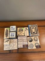 Lot of several new rubber stamps arranged on a wooden surface. Botanical designs including fern, flowers, birds, alphabet letters, and decorative frames.