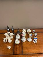 Overview photo of multiple salt and pepper shakers including ceramic floral sets, metal sets, animal-shaped, and novelty figurine shapes arranged on wooden table.