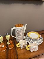 Ceramic teapot, six ironstone plates, cream and sugar boat, two pairs of salt and pepper shakers arranged on table.