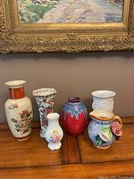 Front view showing all six vases arranged on a wooden surface under a framed painting.