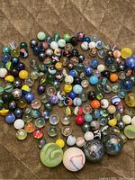 Various vintage marbles scattered on a brown surface, showing different sizes, colors and patterns including swirls, solid colors, and speckled stone-like textures.