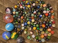 Display of a varied collection of marbles including large, medium, and small sizes laid out on a surface showing different colors and patterns.
