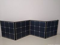 Fully unfolded 4-section solar panel showing black monocrystalline cells with white grid lines, laid flat.