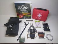 The overall lot contents displayed on a flat surface showing the multi-tool, fire starter, cordage, folding bucket, medical kit, and survival book.