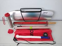 Photo showing the GoSun Sport solar reflector with black metal stand, stainless steel solar water boiler with red silicone lid and handle, silicone clamshell oven mitt, cleaning wand, green scrubby, red silicone lid, and red storage bag.