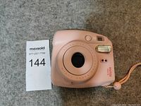 Pink Fujifilm Instax Mini 8 instant film camera on carpet floor with auction lot number card.