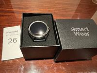 Smart watch placed inside original black box labeled 'Smart Wear' with foam insert.
