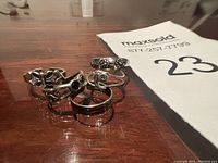 Photo showing five sterling silver toe rings arranged on a wooden surface, featuring various detailed floral and plain band designs.