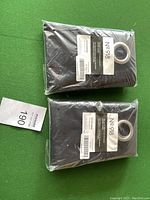 Two black No. 918 eyelet curtains in original plastic packaging on green surface with a lot number card.