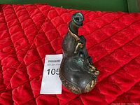 Photo of vintage bronze gourd-shaped decorative item on red quilted fabric surface showing front and handle side.