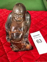Front angled view of a carved buffalo horn laughing Buddha sculpture showing detailed facial features and rounded belly on red background.